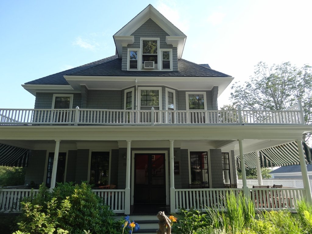 Grey two-storey house with a wide wraparound porch and gardens